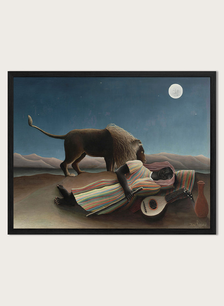 A framed surreal art print depicting a lion standing over a sleeping person wrapped in a striped blanket, with a guitar, vase, and full moon in a night sky. The Sleeping Gypsy by Henri Rousseau is a vintage art print featuring a sleeping traveler, lion, moonlit desert, striped robe, mandolin, and deep blue night sky.