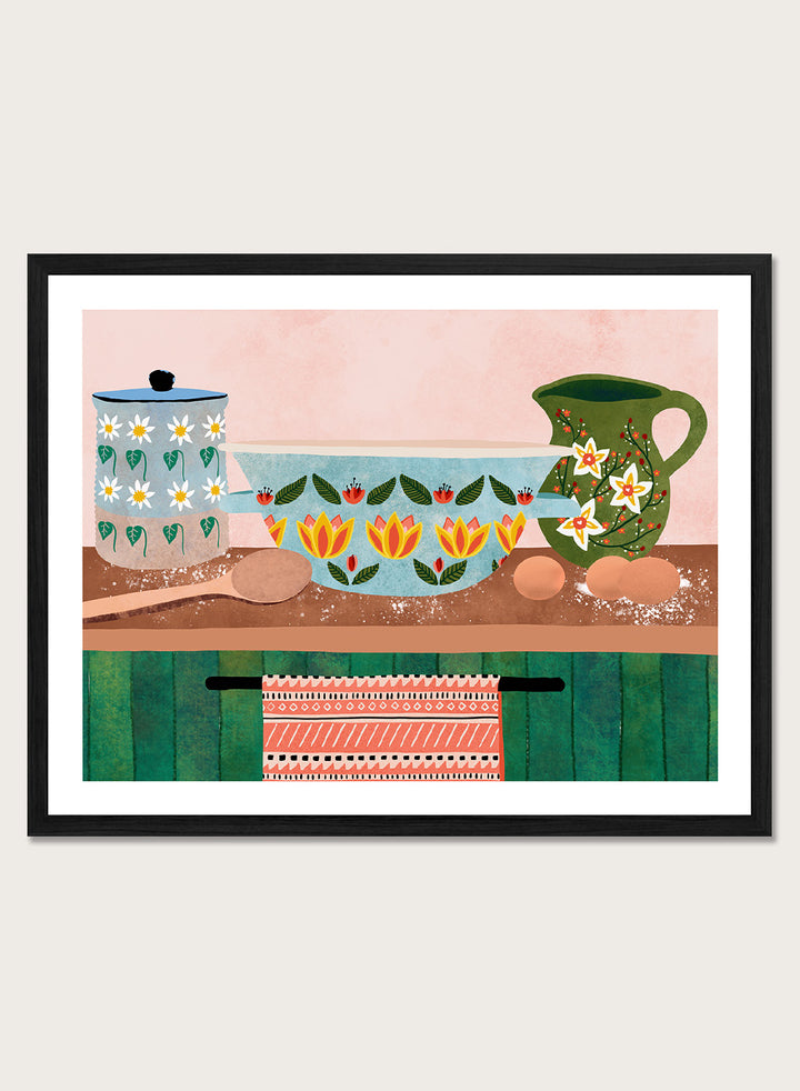 Framed art print featuring a whimsical still life illustration of kitchenware, including a floral-patterned bowl, a green pitcher, eggs, and a patterned towel. Charming Folk Kitchen by Ceyda Alasar kitchen art print featuring painted pottery, floral patterns, wooden spoons, eggs, and colorful folk-inspired decor.