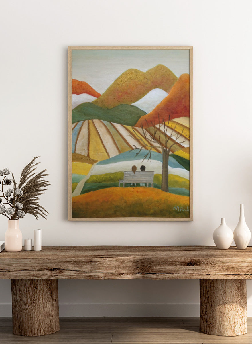 A stylized landscape painting with layered mountains, terraced fields, a bare tree, and two small figures seated on a bench in the foreground. Shop Couple On Autumn Bench by Angeles M. Pomata, an autumn landscape and figurative art print featuring a seated couple, rolling hills, patchwork fields, and warm fall tones.
