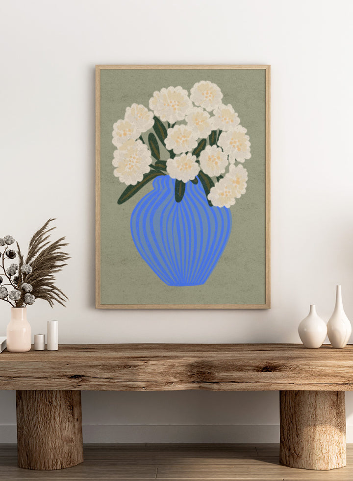 A stylized floral artwork showing a bouquet of off-white flowers with dark green leaves in a blue ribbed vase against a muted sage background. Shop White Blooms Blue Vase by Nikita Jariwala, a floral wall art print poster featuring white flowers in a striped blue vase with modern botanical style.