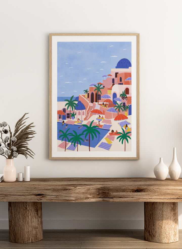A stylized art print depicting a Mediterranean resort scene with palm trees, beach umbrellas, lounge chairs, a swimming pool, and pastel-colored buildings under a light blue sky. Mediterranean Poolside Retreat by Ceyda Alasar travel art print featuring a colorful coastal resort, palm trees, sunbathers, striped umbrellas, and sea views.