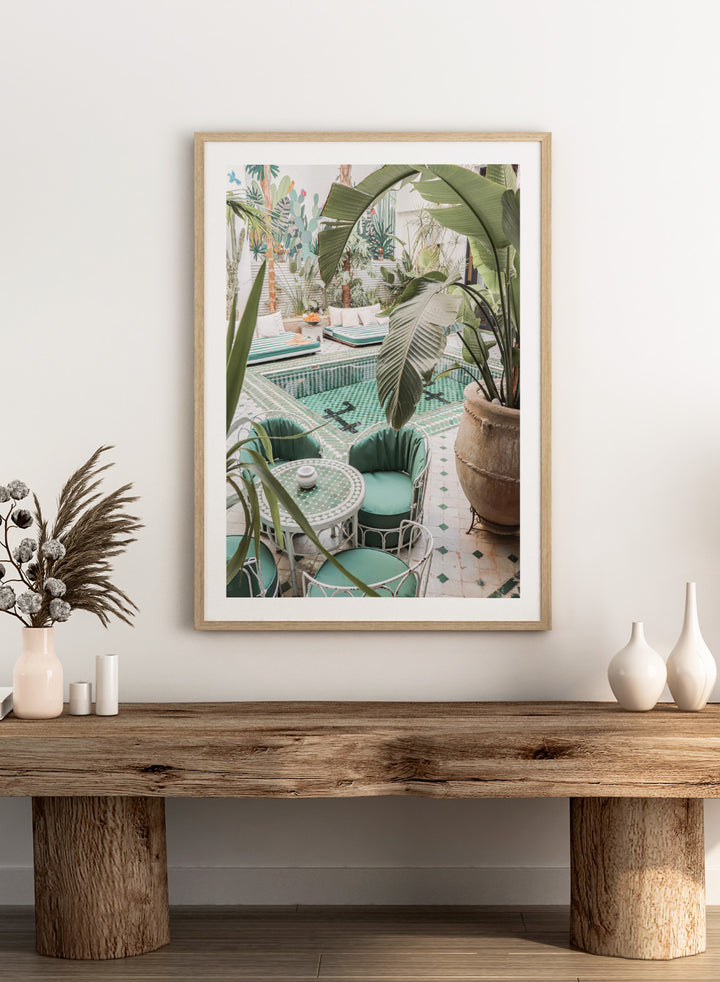 Outdoor patio with pool, green chairs, and potted plants. Green Courtyard Oasis by Henrike Schenk is a Morocco travel photography print showing a lush riad courtyard with green tilework, tropical plants, and poolside interiors.
