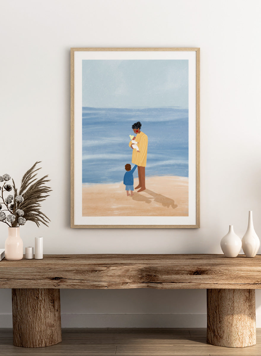 A framed art print featuring an illustration of a man in a yellow striped shirt holding a white dog on a beach next to a child in a blue coat, set against a light blue ocean and pale sky. Family Beach Day by Bea Müller art print featuring a mother with her baby and young child by the sea, created for warm family and coastal decor.