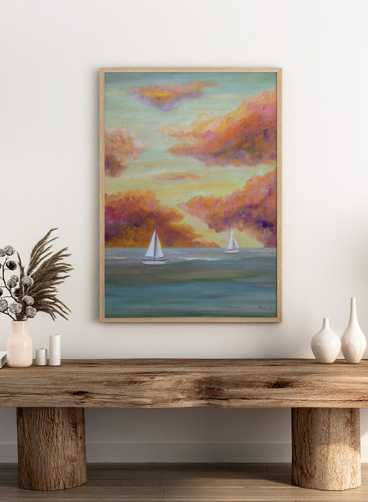 A framed painting of two white sailboats on a calm blue-green sea under a sky filled with soft, painterly clouds in pink, orange, yellow, and purple tones. Shop Sailboat Sunset Sky by Angeles M. Pomata, a coastal landscape art print featuring sailboats, calm water, and a glowing sunset sky.