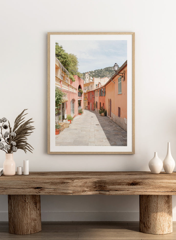 Tiled street with colorful buildings and greenery under a clear blue sky. Colorful Old Town Street by Henrike Schenk is a European travel photography print featuring Mediterranean architecture, pastel buildings, and street wall art.