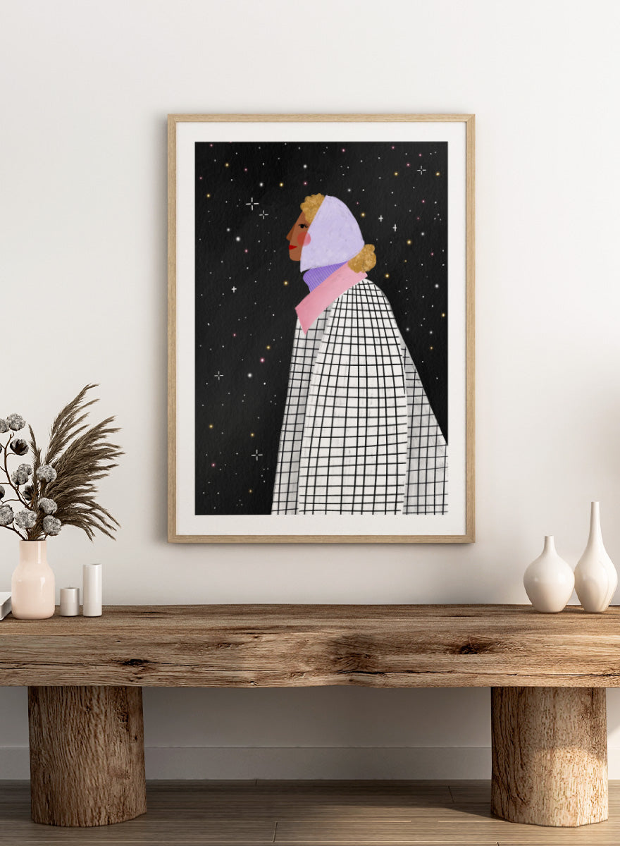 A framed art print featuring a stylized illustration of a woman in profile wearing a white and black checkered cape and a lavender headscarf against a black starry background. Shop Woman Under Starry Night by Bea Müller, a figurative wall art print poster featuring a contemplative woman beneath a star-filled black night sky.