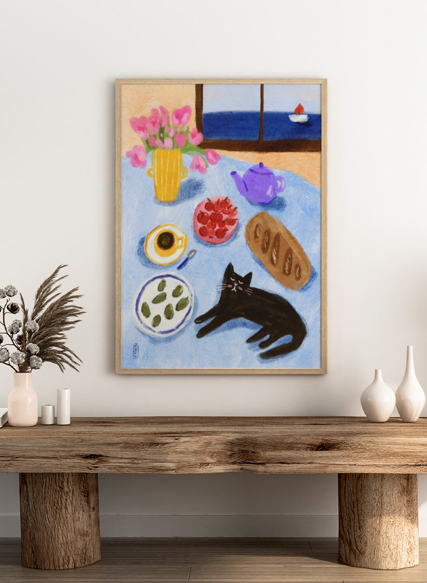 A colorful still life painting of a table scene with pink tulips in a yellow vase, a purple teapot, a bowl of strawberries, a cup of coffee, a loaf of bread, a black cat, and a window view of the sea with a small sailboat. Shop Relaxing Seaside Cat Breakfast by Dirkie Nell, a playful cat and food art print featuring breakfast, flowers, a sailboat, and a seaside view.