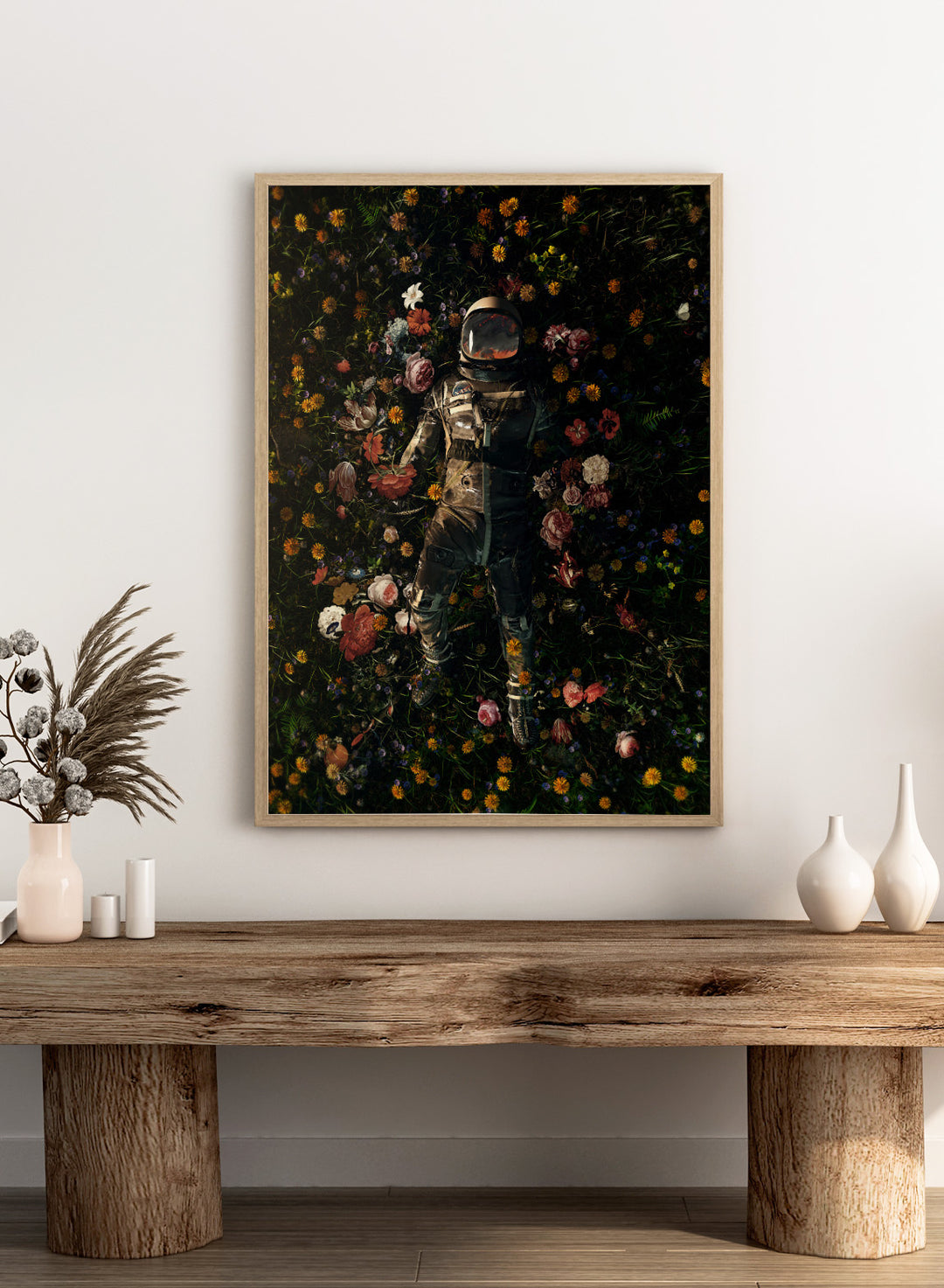 Person in a spacesuit lying on a bed of flowers with a dark background. Cosmic Floral Dream by Nicebleed is a surreal astronaut floral art print featuring a space figure surrounded by flowers, modern aesthetic wall poster.