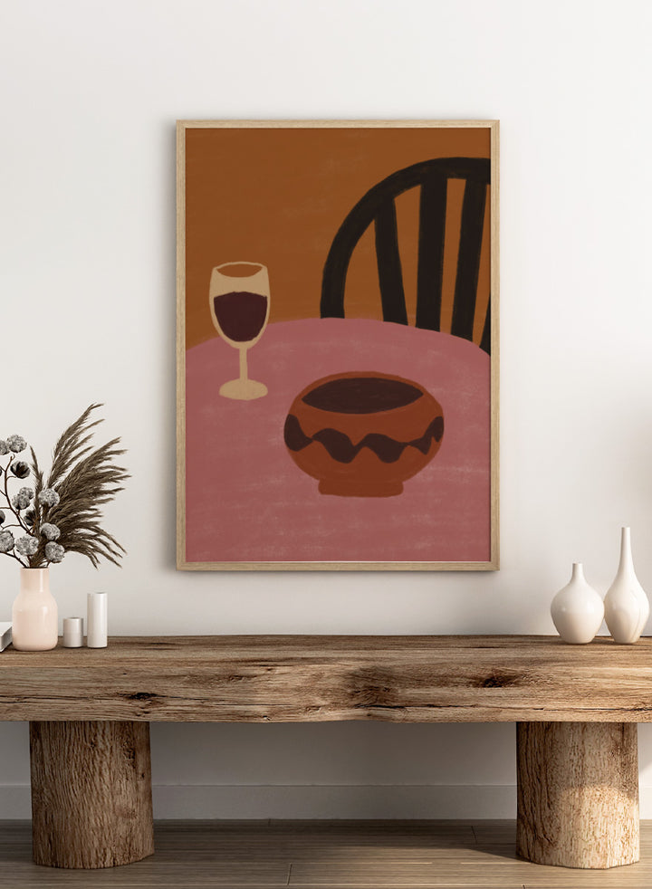 A stylized still life artwork showing a pink table, a dark brown bowl in the foreground, a wine glass with deep red liquid, and a black chair against a warm brown background. Warm Dining Still Life by The Art Concept still life art print featuring red wine, a rounded bowl, pink tabletop, and rich burgundy and rust tones.