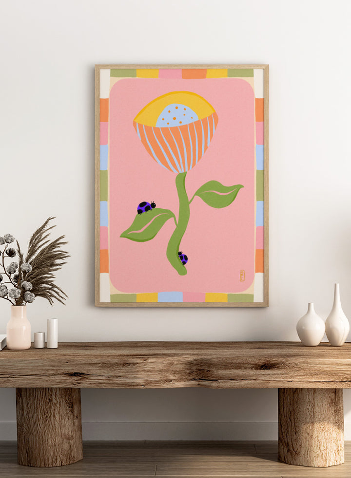 A stylized art print featuring a large flower with a yellow and orange striped bloom, green stem and leaves, and two ladybugs on a pink background with a multicolor border. Shop Pastel Flower Ladybugs by Dirkie Nell, a playful floral and insect art print featuring an oversized pastel flower, purple ladybugs, and a colorful retro border.