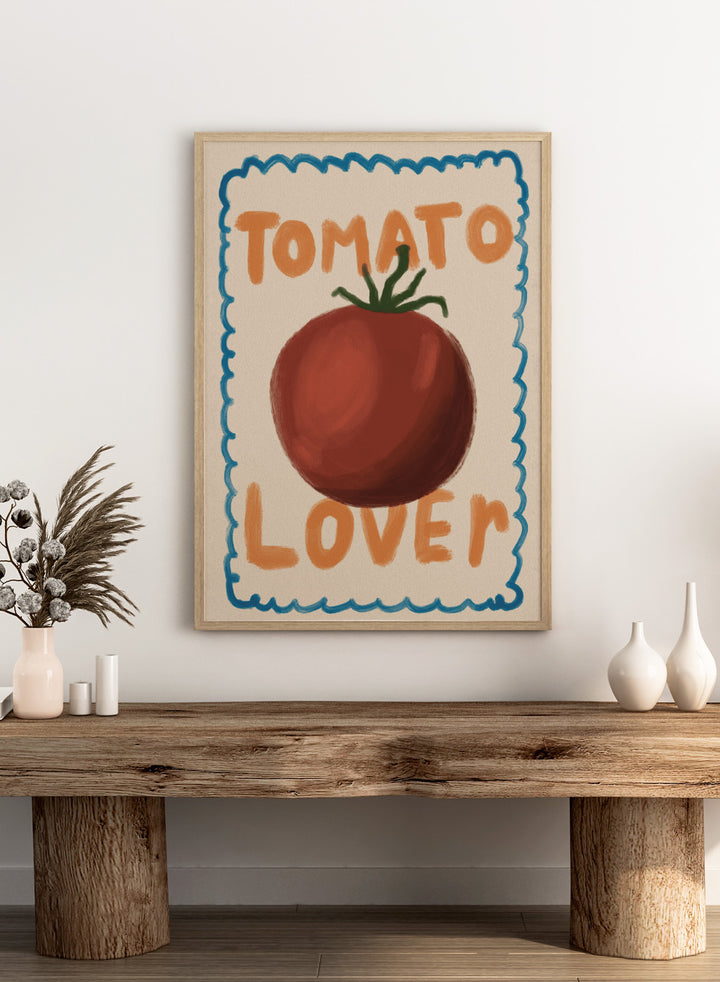An art print featuring a painted red tomato with a green stem, surrounded by a scalloped blue border on a cream background. The words &