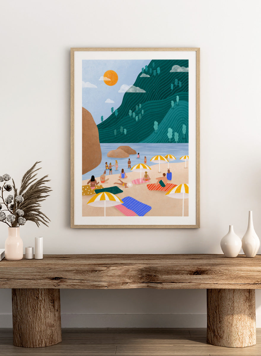 A framed art print featuring a stylized beach scene with a large teal-green mountain, blue water, a yellow sun, and beachgoers under striped umbrellas on a sandy shore. Relaxing Mountain Beach by Bea Müller coastal art print featuring swimmers, striped towels, yellow umbrellas, and a sweeping teal mountain.