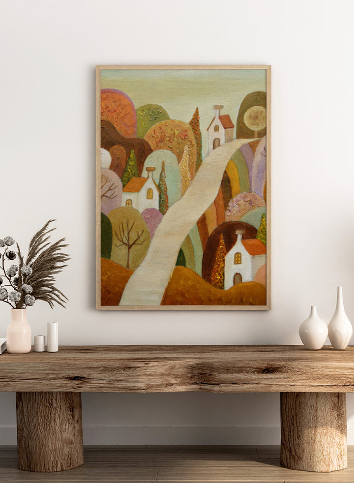 A stylized landscape painting featuring small white houses with orange roofs, rolling hills in earthy tones, and a pale winding path through the scene. Shop Whimsical Village Path by Angeles M. Pomata, an autumn landscape art print featuring a winding road, white village houses, rounded hills, and warm earthy tones.