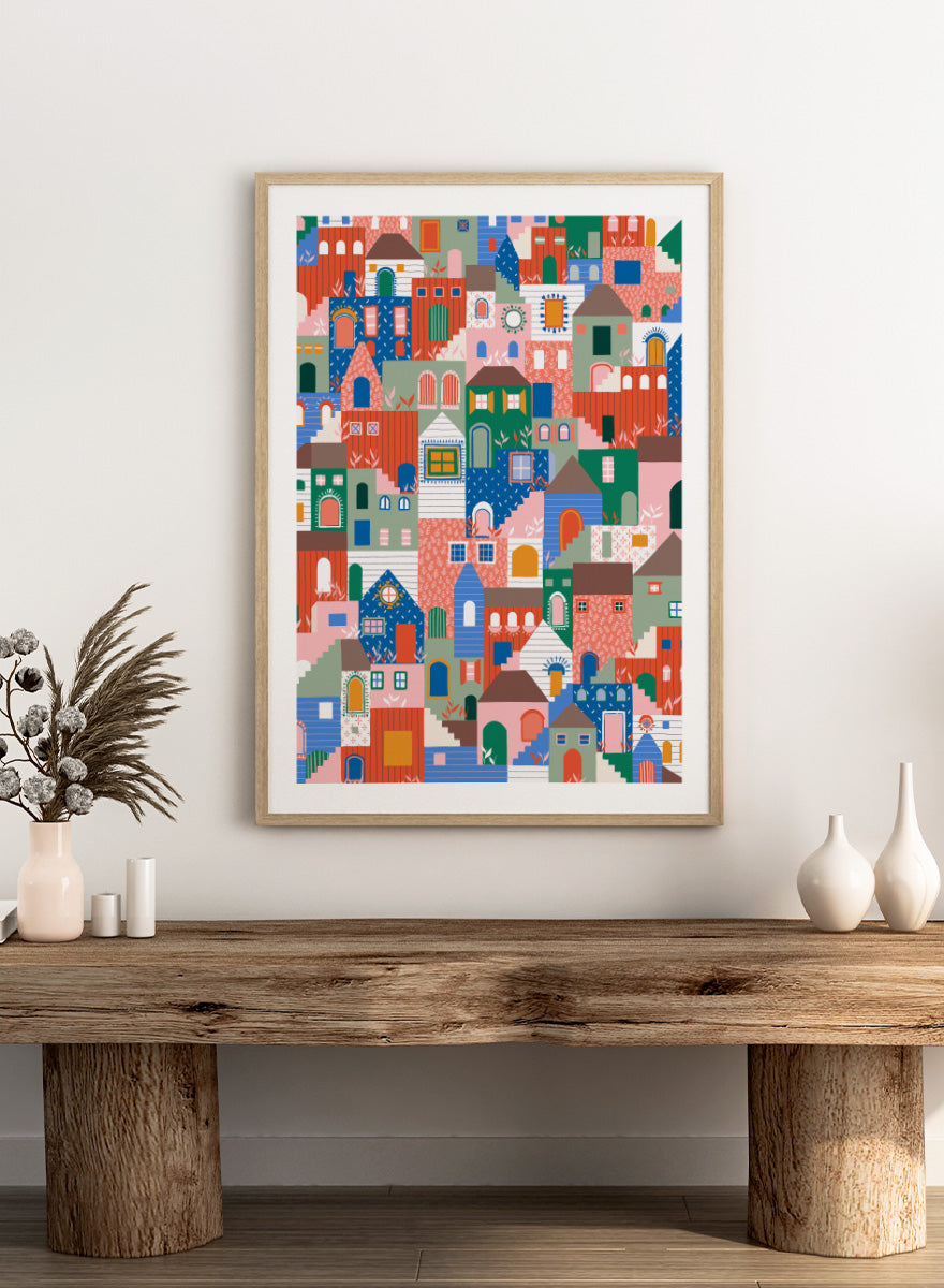 A colorful art print featuring a dense, stylized illustration of houses and buildings in a playful, patterned village scene. Whimsical Cityscape Charm by Ceyda Alasar city art print featuring stacked colorful houses, patterned walls, winding stairs, and playful architectural details.