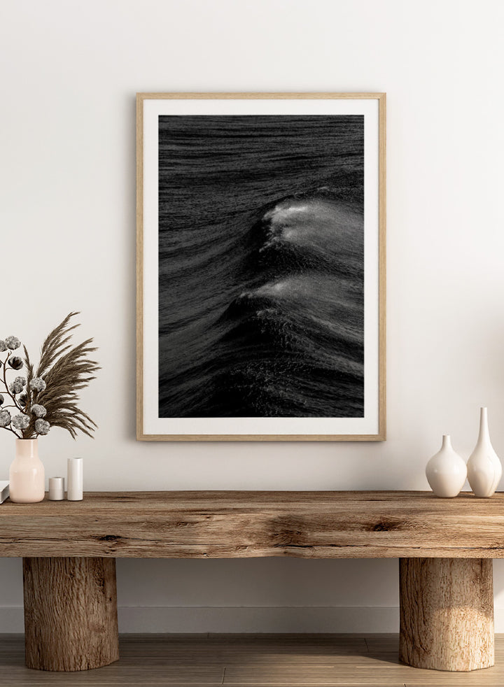 Black and white fine art photographic print of ocean waves, featuring a dramatic wave crest with white foam against dark textured water. Night Wave Cascade by Shot by Clint black-and-white ocean photography print featuring dark rolling waves, sea spray, and dramatic natural movement.