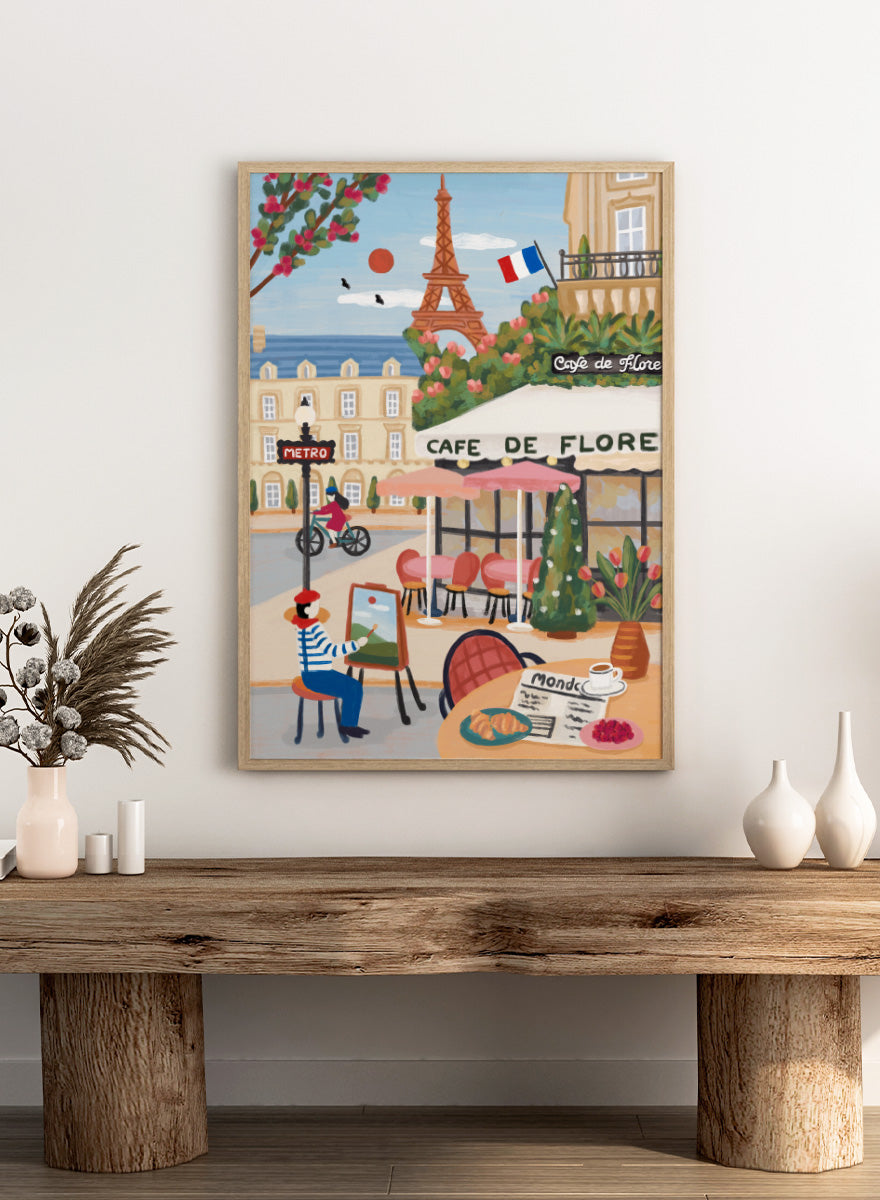 A colorful illustrated Paris street scene with the Eiffel Tower, a cafe exterior labeled Cafe de Flore, a cyclist, a seated painter, flowers, and a French flag. Shop Paris Cafe Life by Nidhi Kachhadiya, a colorful Paris wall art print inspired by French café culture, the Eiffel Tower, and charming European city life.