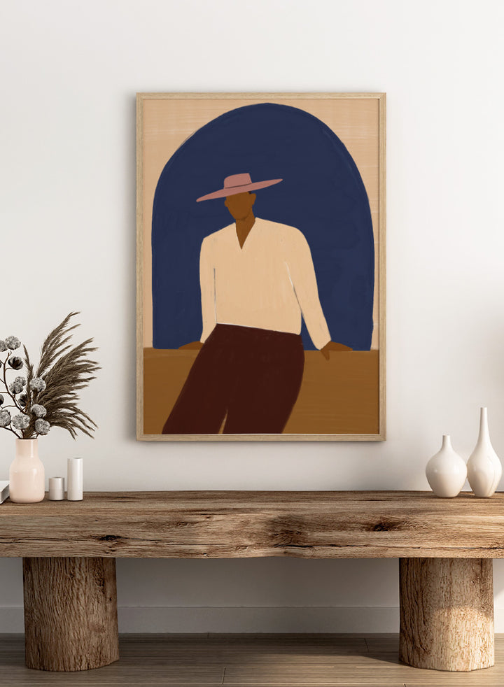 A stylized art print depicting a seated figure in a wide-brimmed pink hat, cream shirt, and dark brown trousers against a large dark blue arch on a beige background. Man In Blue Arch by The Art Concept portrait art print featuring a lone figure beneath a deep blue arch in warm earthy tones.