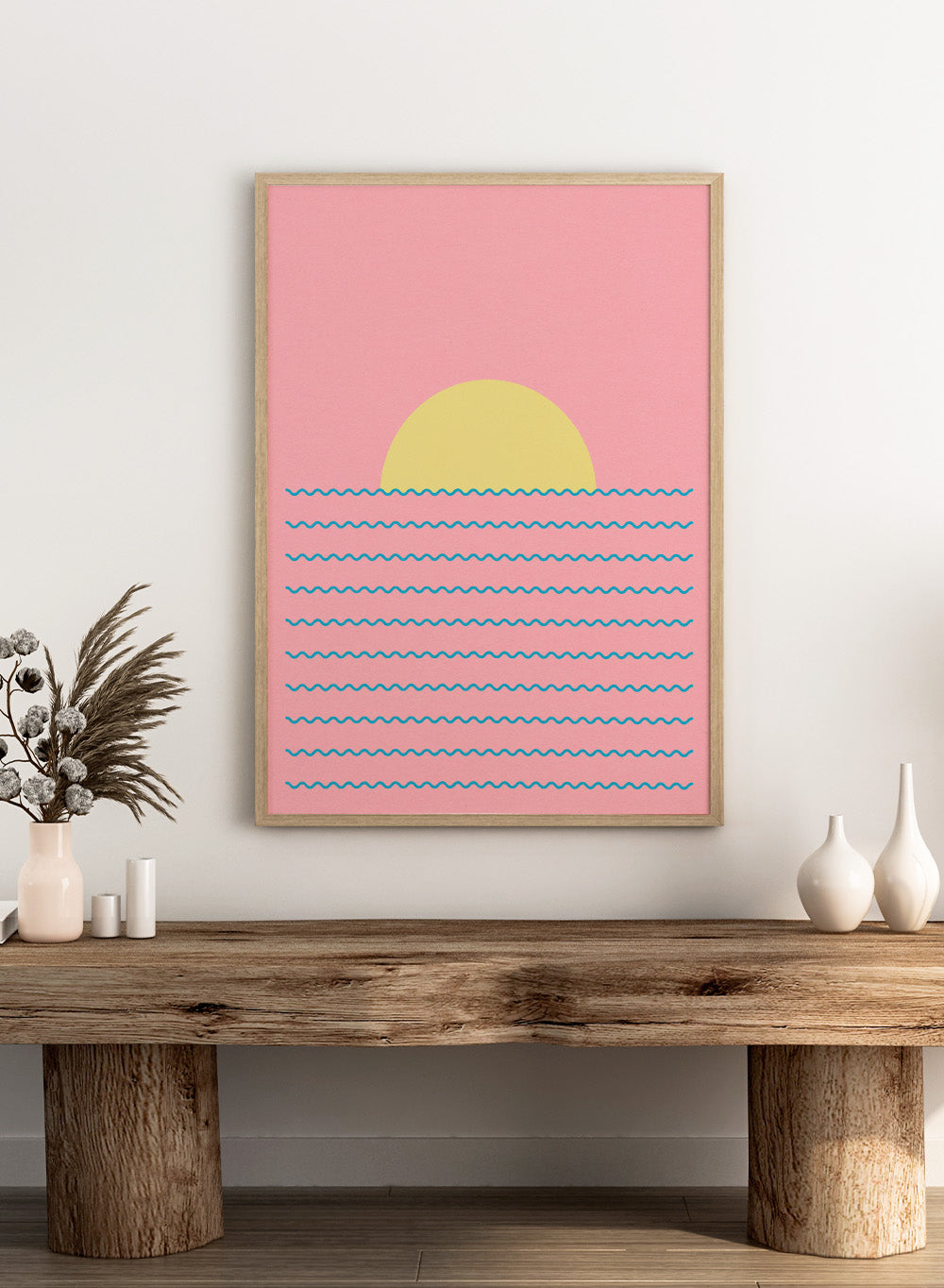 Simplified illustration of a sunset over water with blue waves on a pink background. Every Day the Sun Rises by Rosi Feist is a minimalist sun and waves art print with pink sky. Officially licensed modern poster with framing.