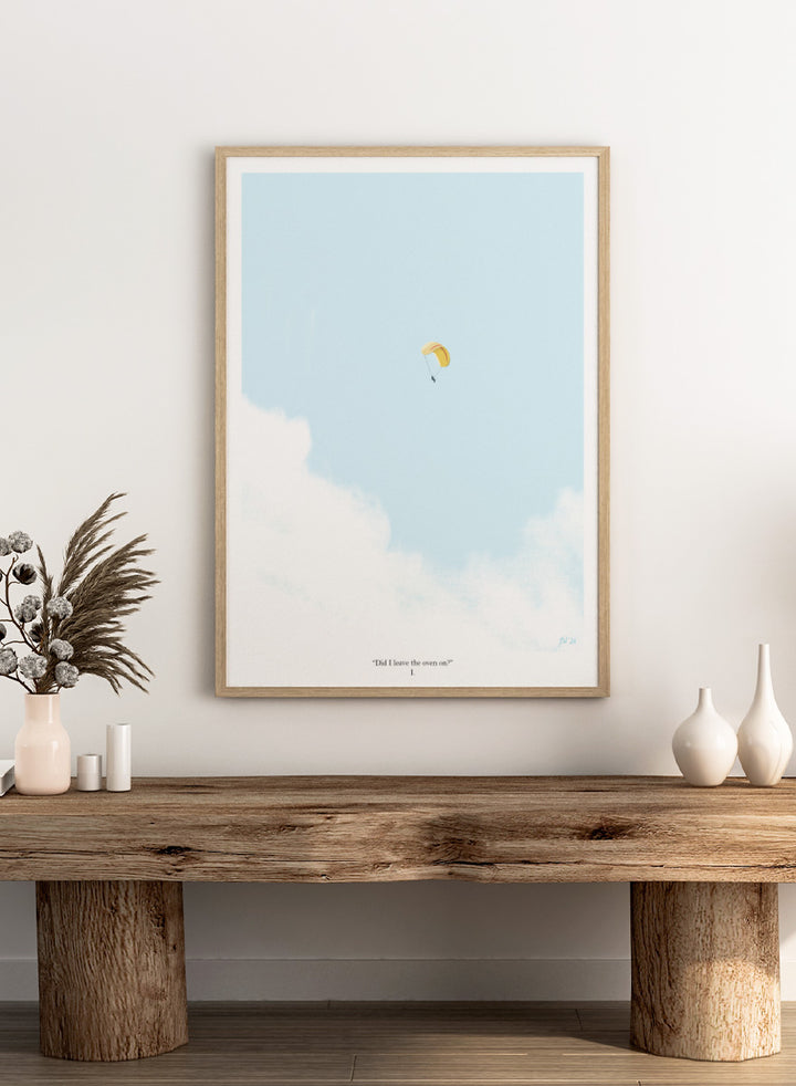A minimalist art print featuring a light blue sky with white clouds and a small yellow-and-white parachute near the center, framed by a black border with the quote &