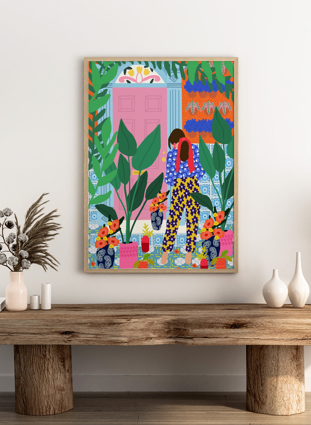 Illustration of a person in colorful pants standing in front of a pink door with plants and flowers. Floral Oasis Retreat by Rafaela Mascaro art print featuring woman in lush garden doorway, colorful plants, patterned tiles, and vibrant contemporary botanical wall art poster.