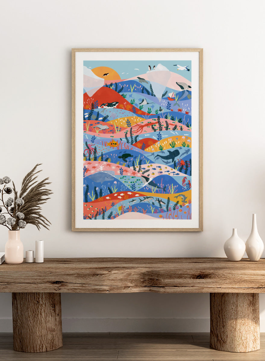 A colorful illustrated art print featuring stylized mountains, sea life, and coastal scenery in layered wavy bands of blue, pink, orange, yellow, and green. Vibrant Ocean Life by Ceyda Alasar ocean art print featuring whales, sharks, rays, turtles, coral reefs, sea plants, and colorful marine life.