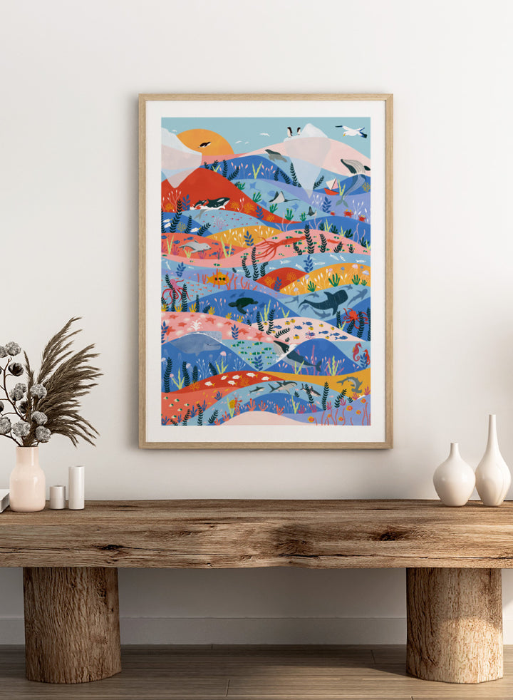 A colorful illustrated art print featuring stylized mountains, sea life, and coastal scenery in layered wavy bands of blue, pink, orange, yellow, and green. Vibrant Ocean Life by Ceyda Alasar ocean art print featuring whales, sharks, rays, turtles, coral reefs, sea plants, and colorful marine life.