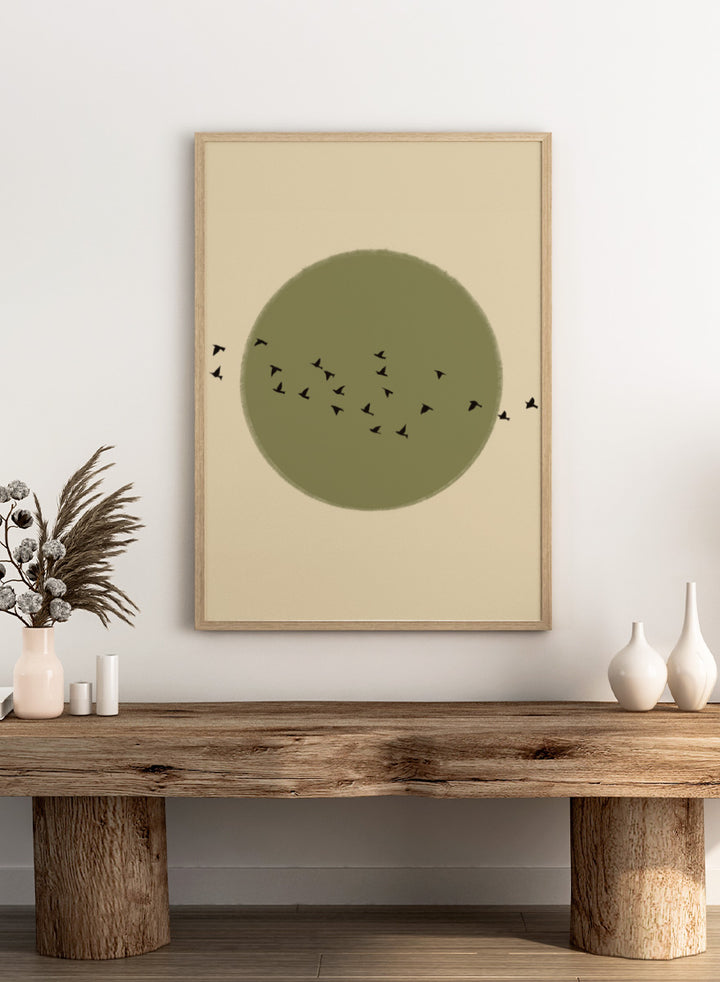 Minimalist art print featuring a large olive green circle with small black bird silhouettes flying across it, set against a warm beige background. Graceful Birds Soaring by The Art Concept is a minimalist bird art print featuring black birds in flight across an olive green circle and warm cream background.