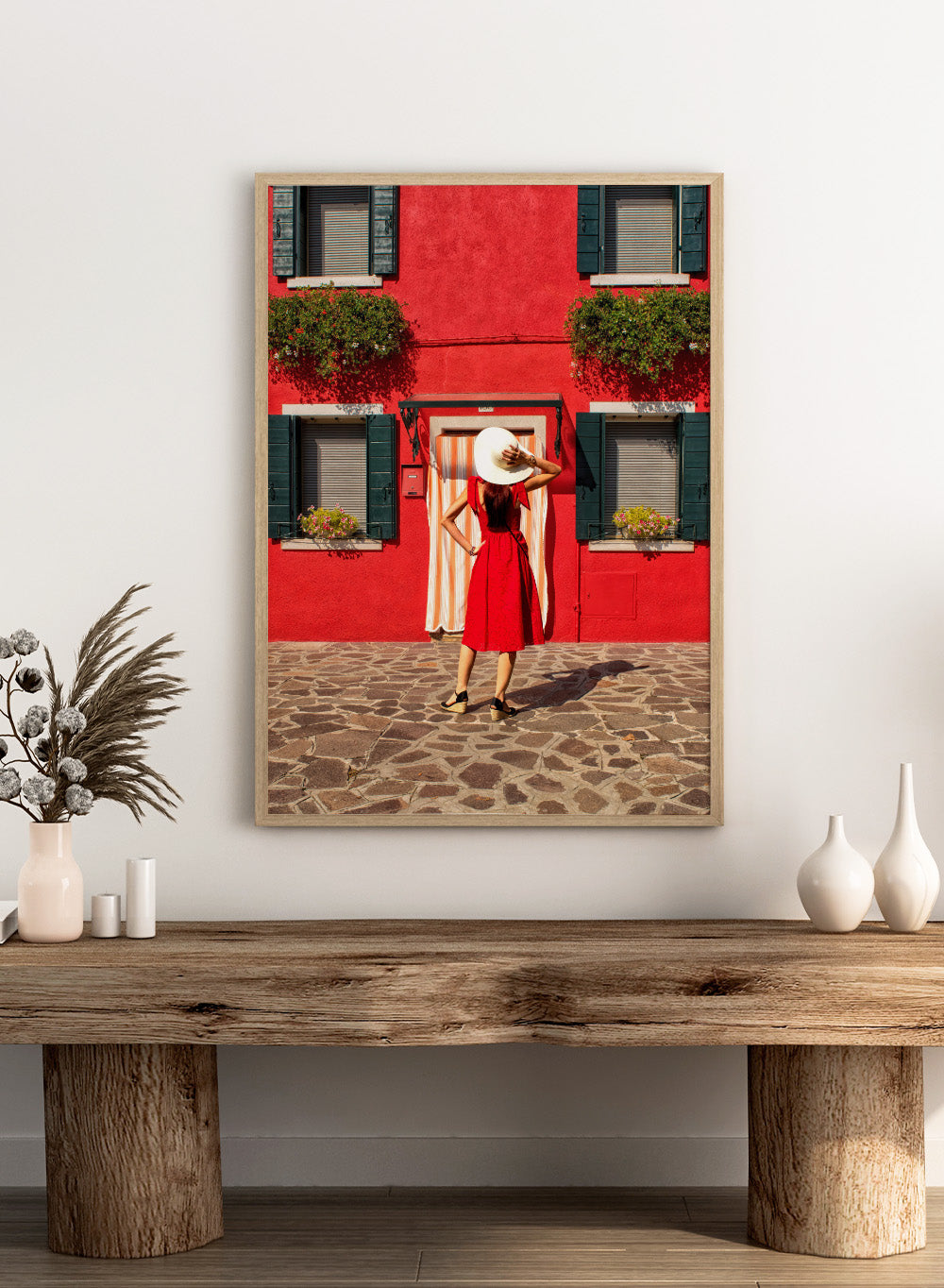 Woman in a red dress and white hat standing in front of a red wall with green shutters. Red Art Print by Anette Ohlendorf featuring a woman in a red dress standing against a red building. Officially licensed travel photography with strong color and symmetry.