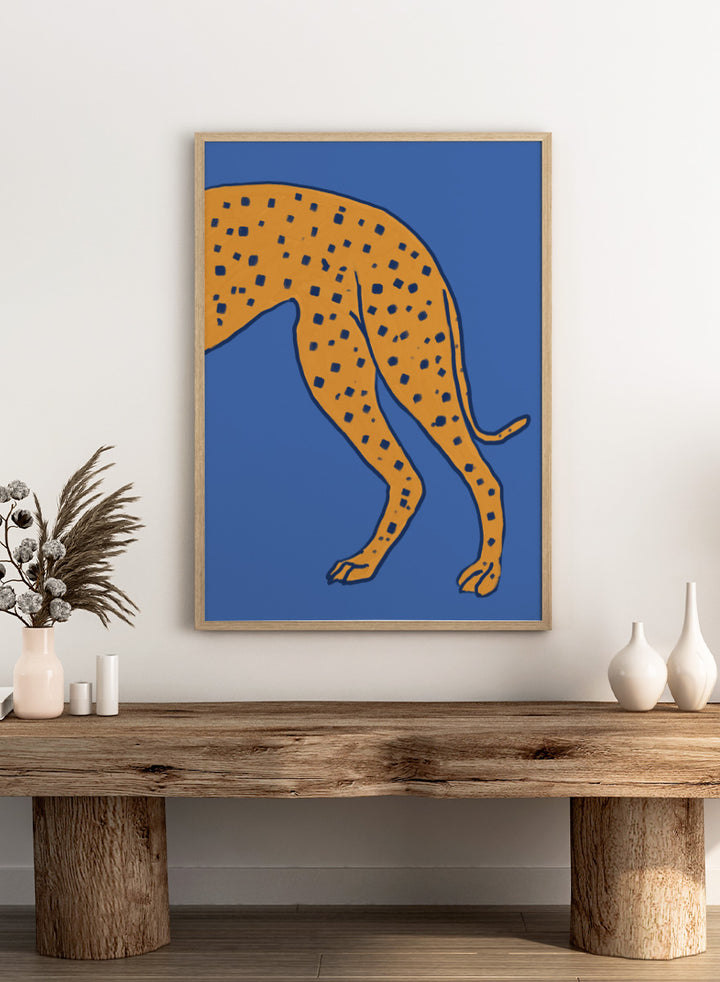 A stylized illustration of a spotted big cat, cropped to show the torso and hind legs, in orange with dark blue spots on a solid blue background. Spotted Cheetah on Blue by The Art Concept animal art print featuring a cropped golden cheetah with deep blue spots against a bold blue background.