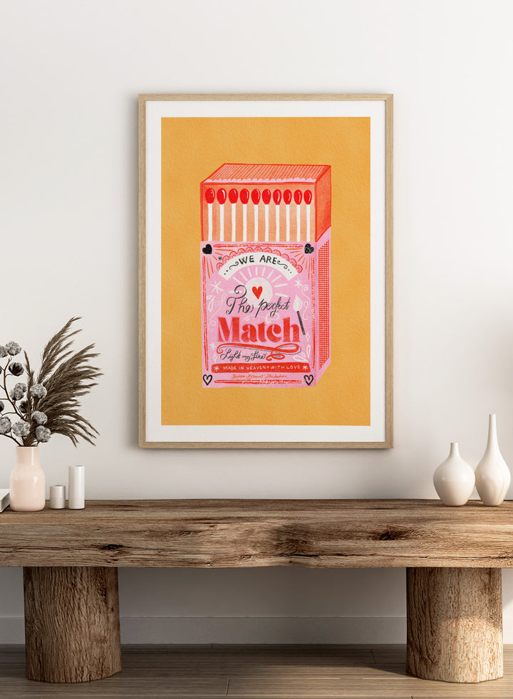 Illustration of a matchbox with 'We are the perfect match' text on a yellow background. Match Box, The Perfect Match by Baroo Bloom is a playful love-themed art print featuring a pink illustrated matchbox. Officially licensed wall poster with optional framing.