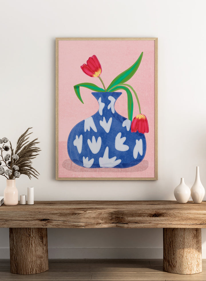 Blue vase with white abstract patterns and red tulips on a pink background. Tulip in Vase by Raissa Oltmanns fine art print featuring bold red tulip, blue patterned vase, modern contemporary floral wall decor poster.