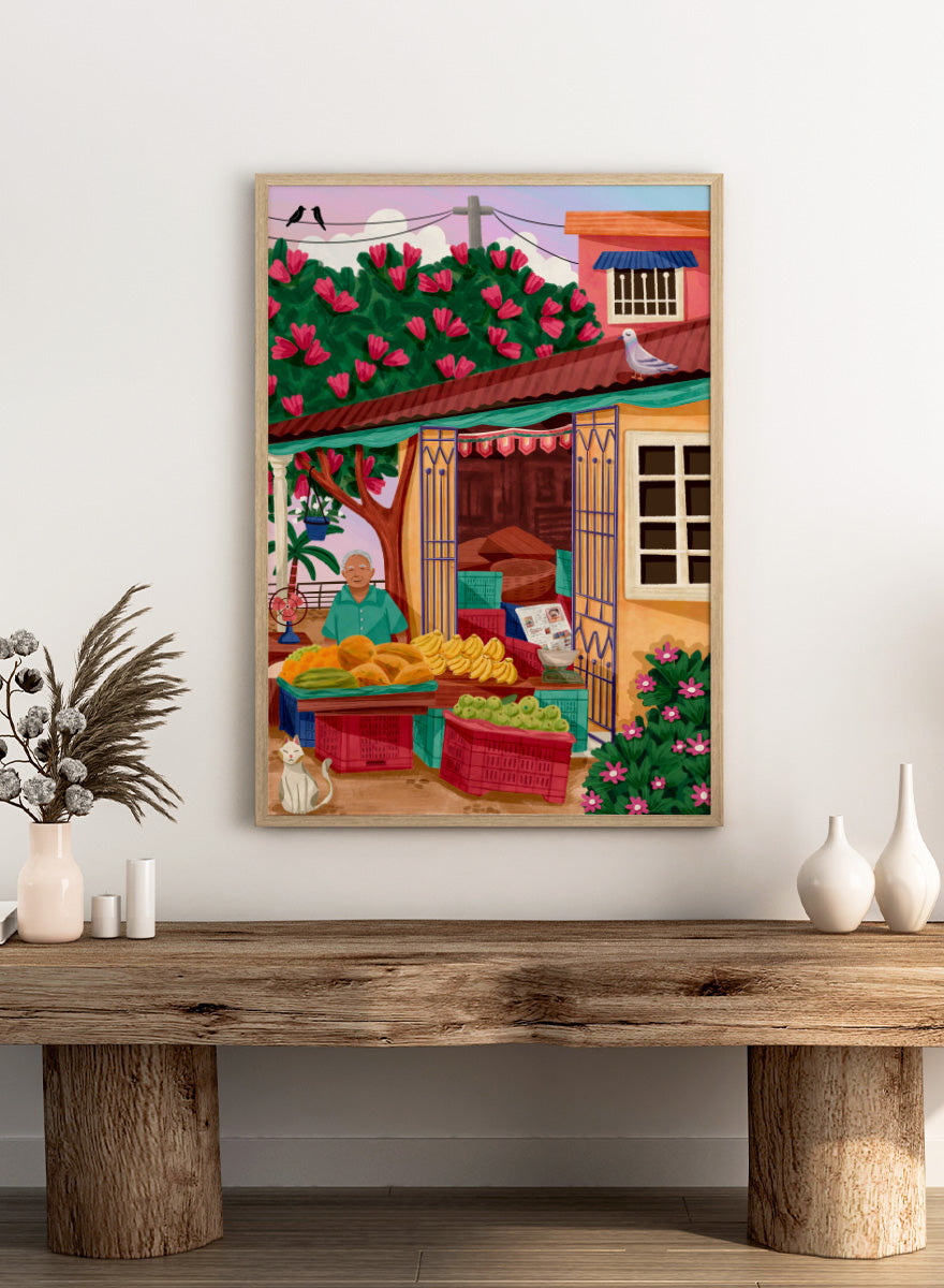 A colorful illustrated street market scene with a vendor standing behind tables of fruit and vegetables, a flowering tree, a house with pink flowers, crates, a pigeon on the roof, birds in the sky, and a white cat in the lower left. Colorful fruit stand art print by Nidhi Kachhadiya with fresh produce, floral details, and market charm. A cheerful print for kitchen or dining spaces.