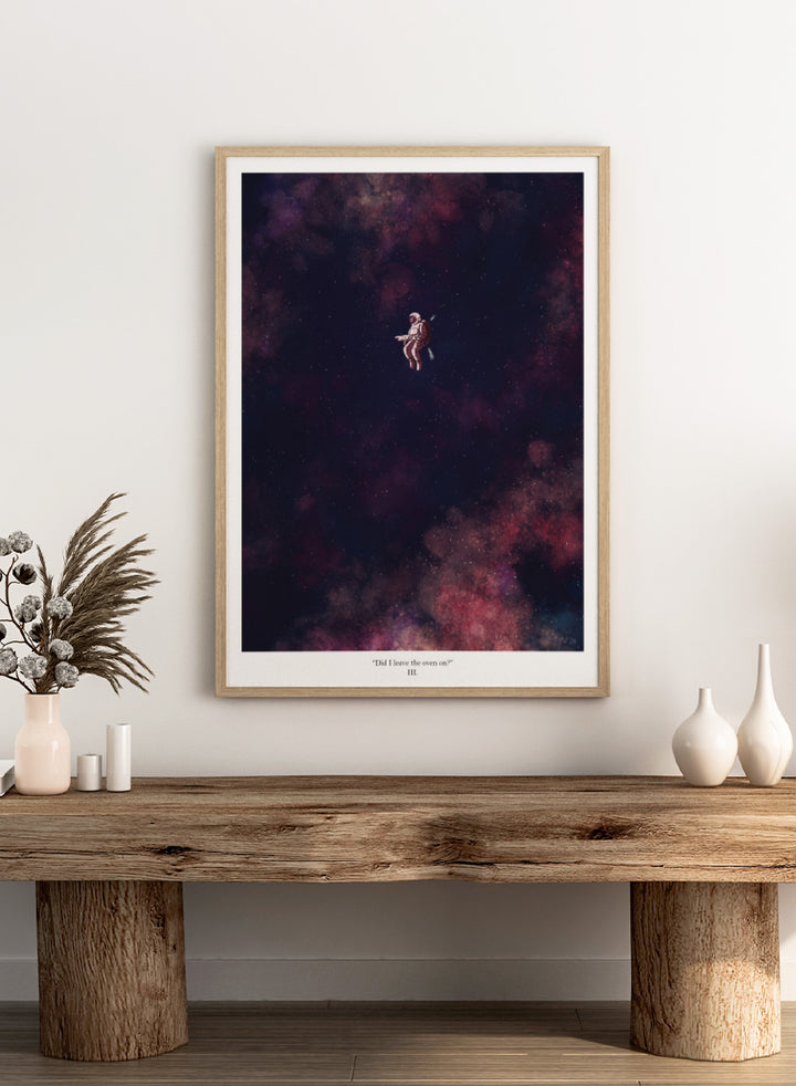 A framed art print featuring an astronaut floating in a starry outer space scene with deep purple, pink, and blue nebulae. The print has a white border with the text &
