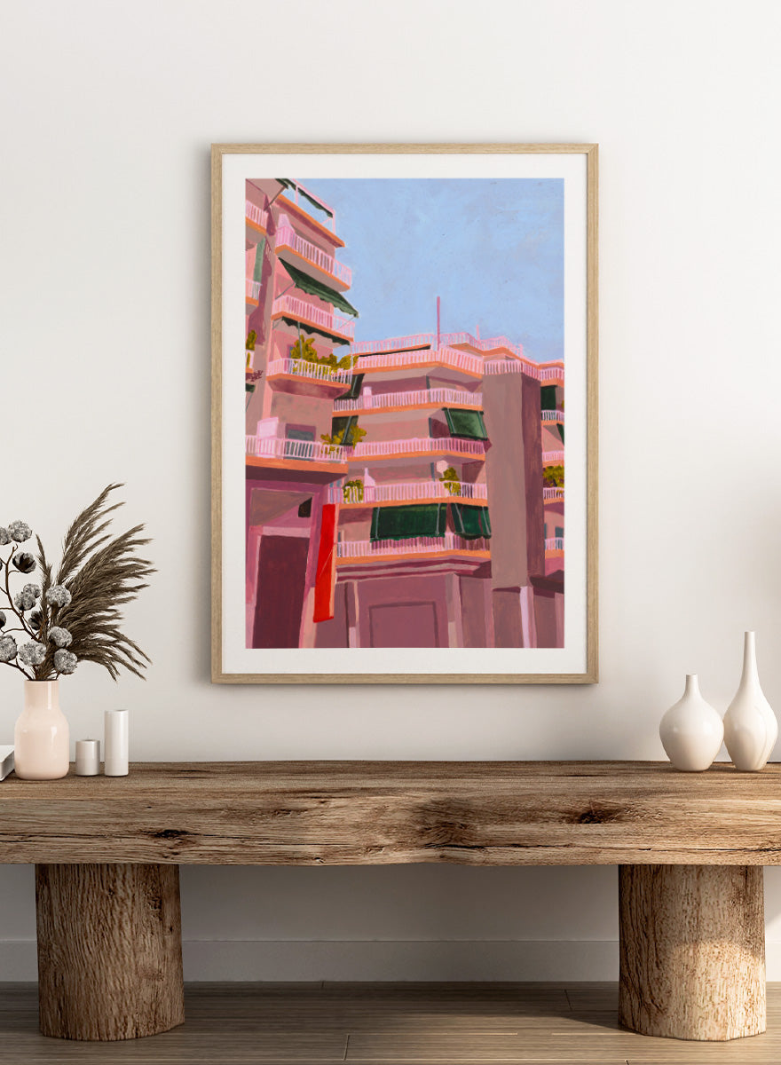 Shop Pink City Balconies by Sophia Novosel, a colorful city wall art print poster featuring pink apartment buildings, green awnings, balconies, and blue sky.
