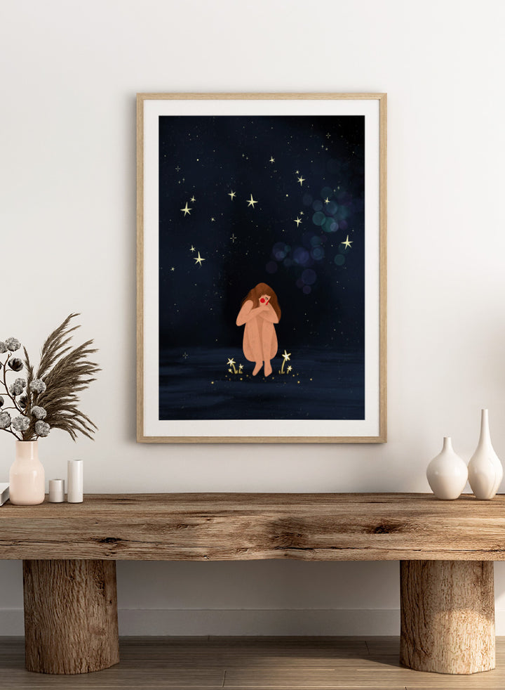 A framed art print featuring a whimsical illustration of a girl sitting on a dark blue starry night sky. Shop Starlit Solitude by Bea Müller, a figurative wall art print poster featuring a solitary woman beneath a star-filled night sky in deep blue tones.