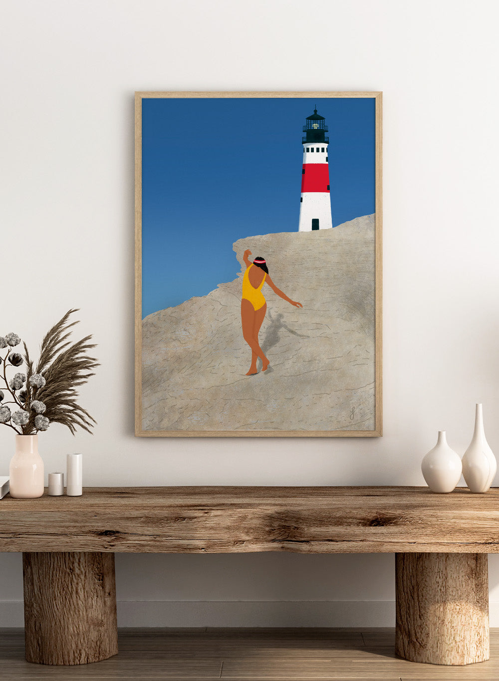 Woman in a yellow swimsuit standing on a rocky outcrop with a lighthouse in the background. My Beach by Jota de Jai is a modern coastal wall art print featuring a woman in a yellow swimsuit and a lighthouse. Officially licensed fine art poster with optional wood frame.