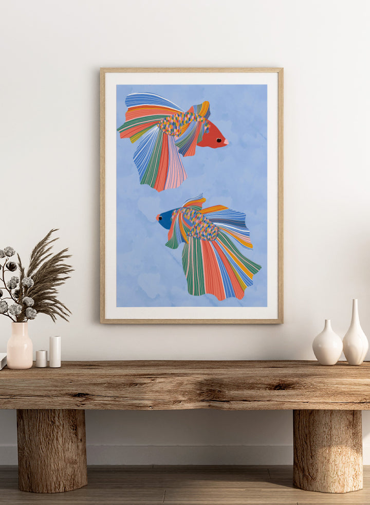 A framed art print featuring two stylized betta fish with vibrant, multicolored striped fins and bodies on a light blue water-like background. Colorful Betta Duo by Ceyda Alasar fish art print featuring two patterned betta fish with flowing fins in bright coral, blue, green, pink, and yellow.