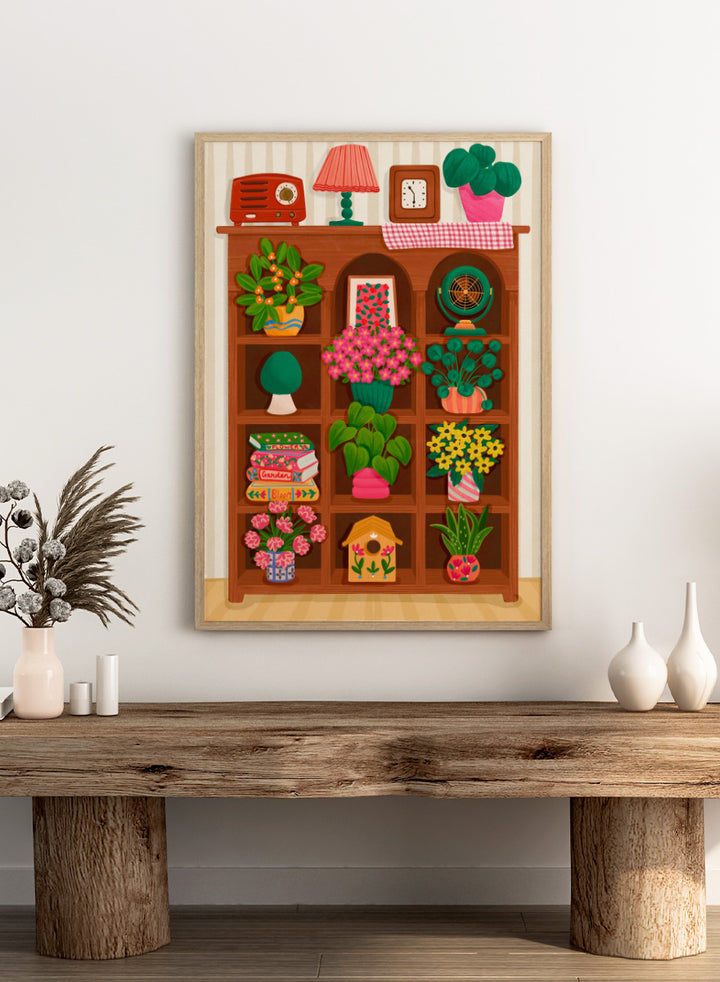 A colorful cartoon-style illustration of a wooden bookshelf filled with potted plants, flowers, books, a lamp, a clock, a radio, and other home decor items, set against a striped wall. Shop Cozy Botanical Shelf by Nidhi Kachhadiya, a colorful botanical wall art print featuring houseplants, flowers, vintage decor, and warm green and pink tones.