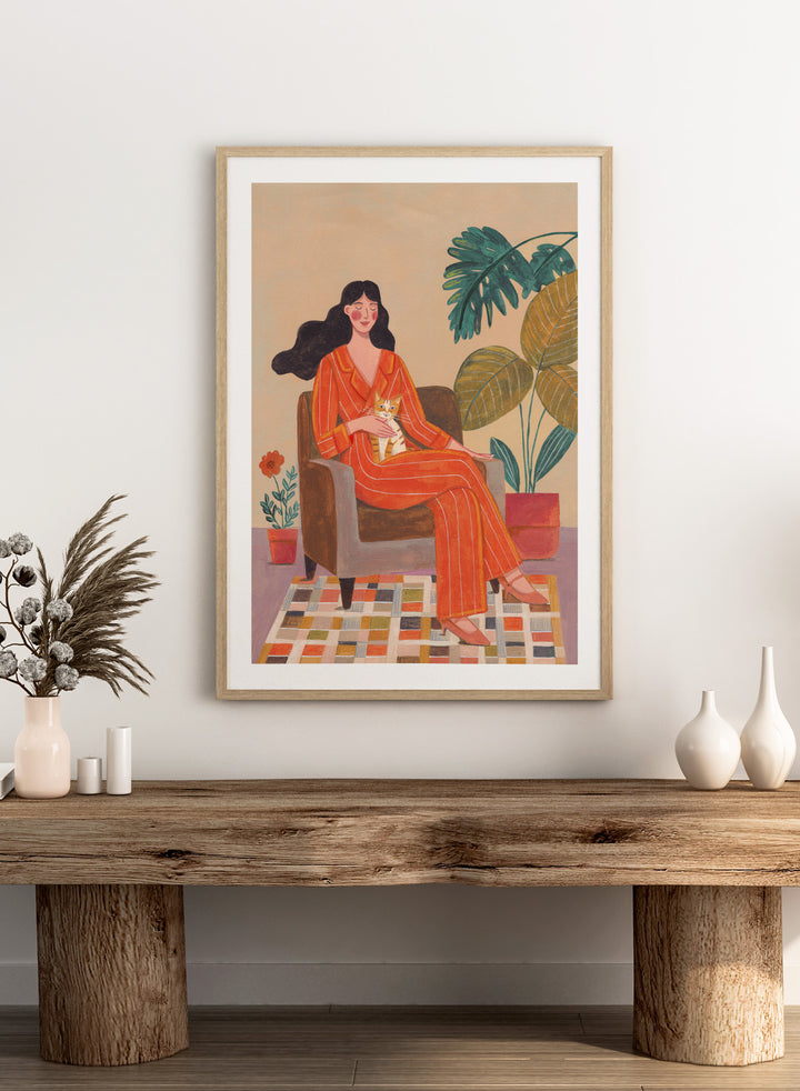 Illustration of a woman in an orange outfit sitting in a chair with plants around her. Cozy Home with Cat by Caroline Bonne Müller is a fine art print and wall poster featuring a woman in an orange outfit sitting with a cat in a warm, plant-filled interior.