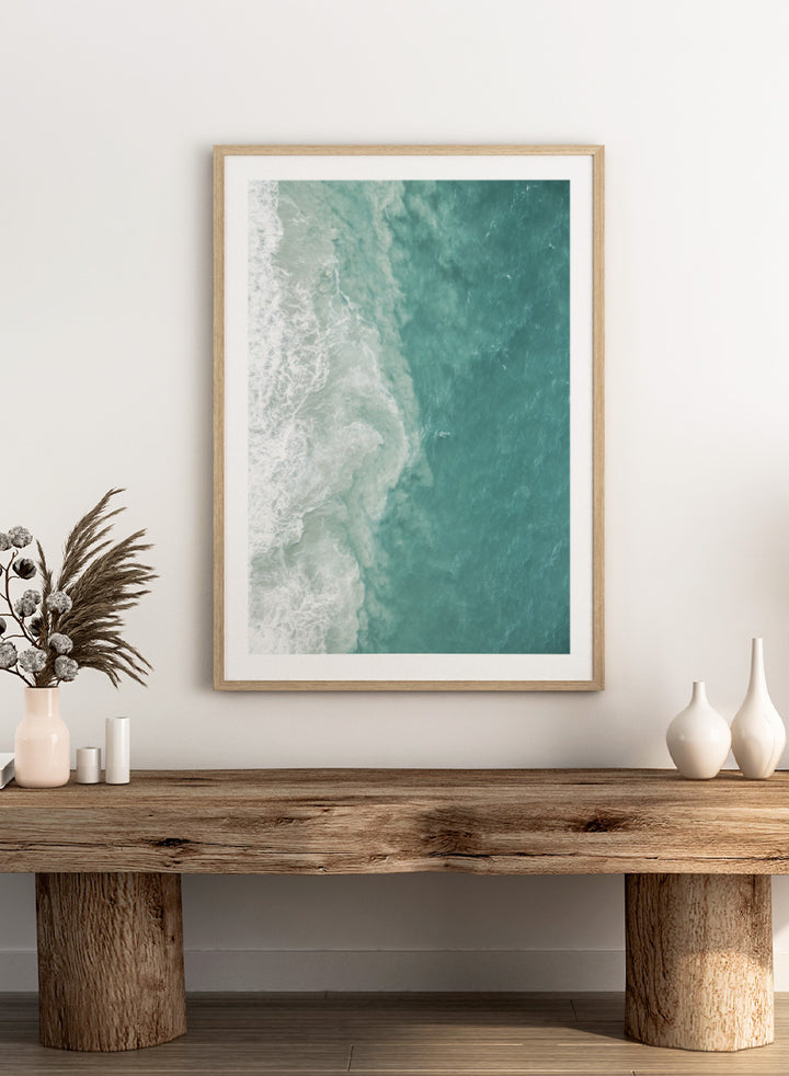 A framed aerial photograph of ocean waves, showing white foam breaking into turquoise and teal water. Ocean’s Edge by Shot by Clint aerial ocean photography print featuring turquoise water, white surf, and layered coastal movement.