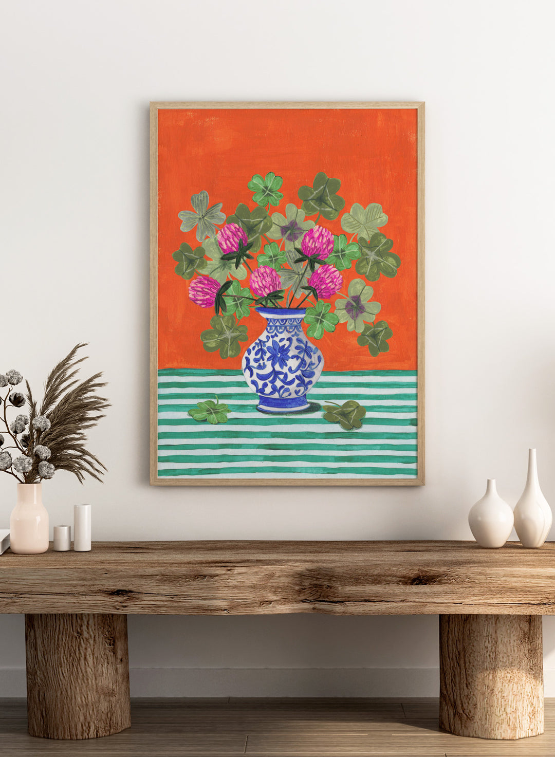 Vase with pink flowers and green leaves on a red and green striped background. Vibrant Clover Still Life by Caroline Bonne Müller is a fine art print and wall poster featuring clover leaves, pink flowers, and a blue vase on a striped table.