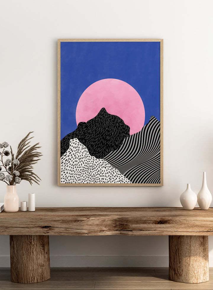 Artistic depiction of mountains with a pink moon in a blue sky. Surreal Peaks View by Elena Ristova is a minimalist abstract landscape print with bold mountains and a pink sun. Officially licensed wall poster with framing.