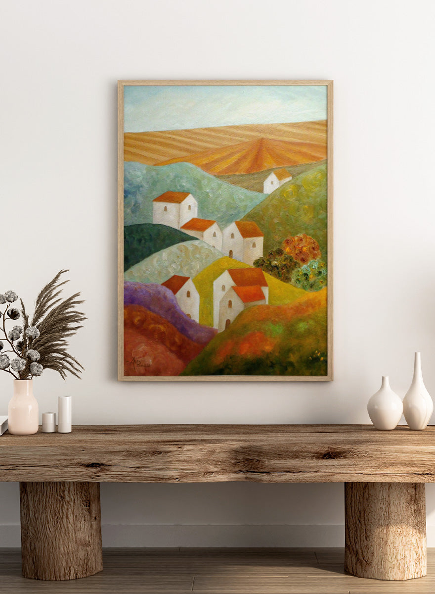 A colorful landscape painting featuring white houses with orange-red roofs nestled among rolling hills in shades of green, purple, yellow, and orange, with a plowed field under a pale sky in the background. Shop Colorful Hillside Village by Angeles M. Pomata, an autumn countryside art print featuring white houses, rolling hills, warm fields, and earthy color.
