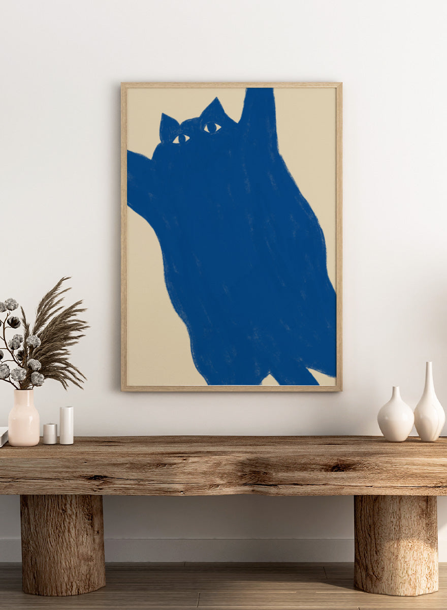 A minimalist art print featuring a bold blue cat silhouette with white eyes on a warm beige background. Playful Blue Cat by The Art Concept is a modern cat art print featuring a bold blue feline, oversized crop, and warm cream background.