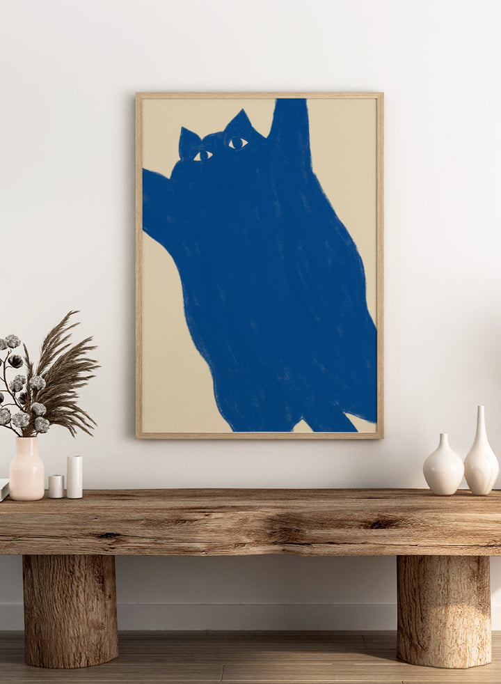 A minimalist art print featuring a bold blue cat silhouette with white eyes on a warm beige background. Playful Blue Cat by The Art Concept is a modern cat art print featuring a bold blue feline, oversized crop, and warm cream background.
