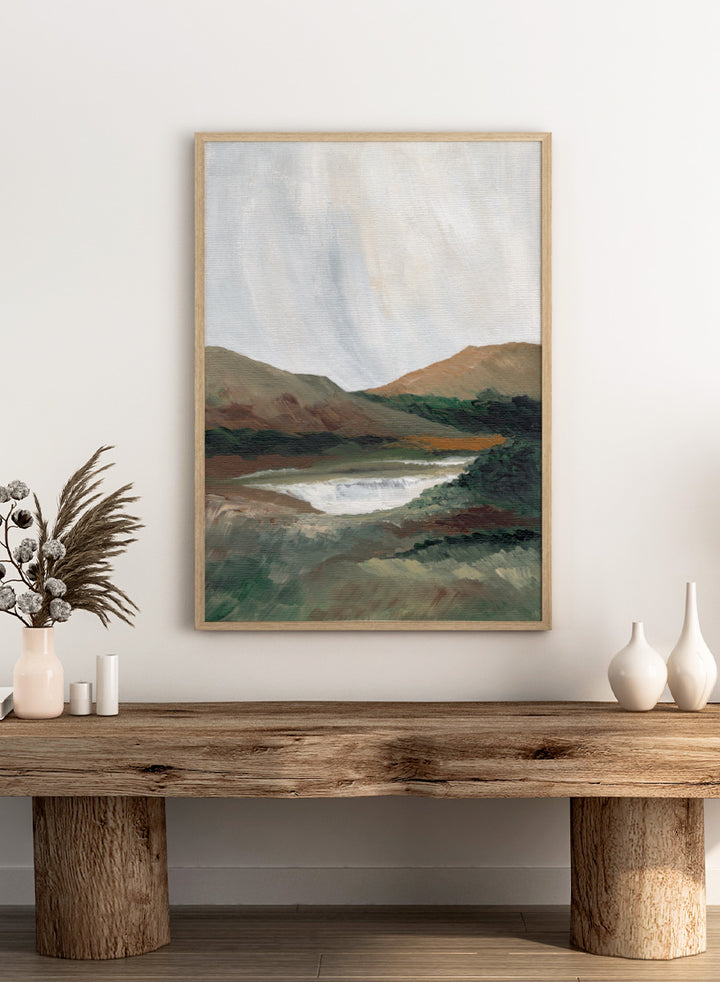 An impressionistic landscape painting of a river or waterfall flowing through a valley, with brown and green hills under a pale sky. Shop Serene Mountain Lake by Nikita Jariwala, a mountain landscape wall art print poster featuring a peaceful lake, wooded hills, and soft green tones.