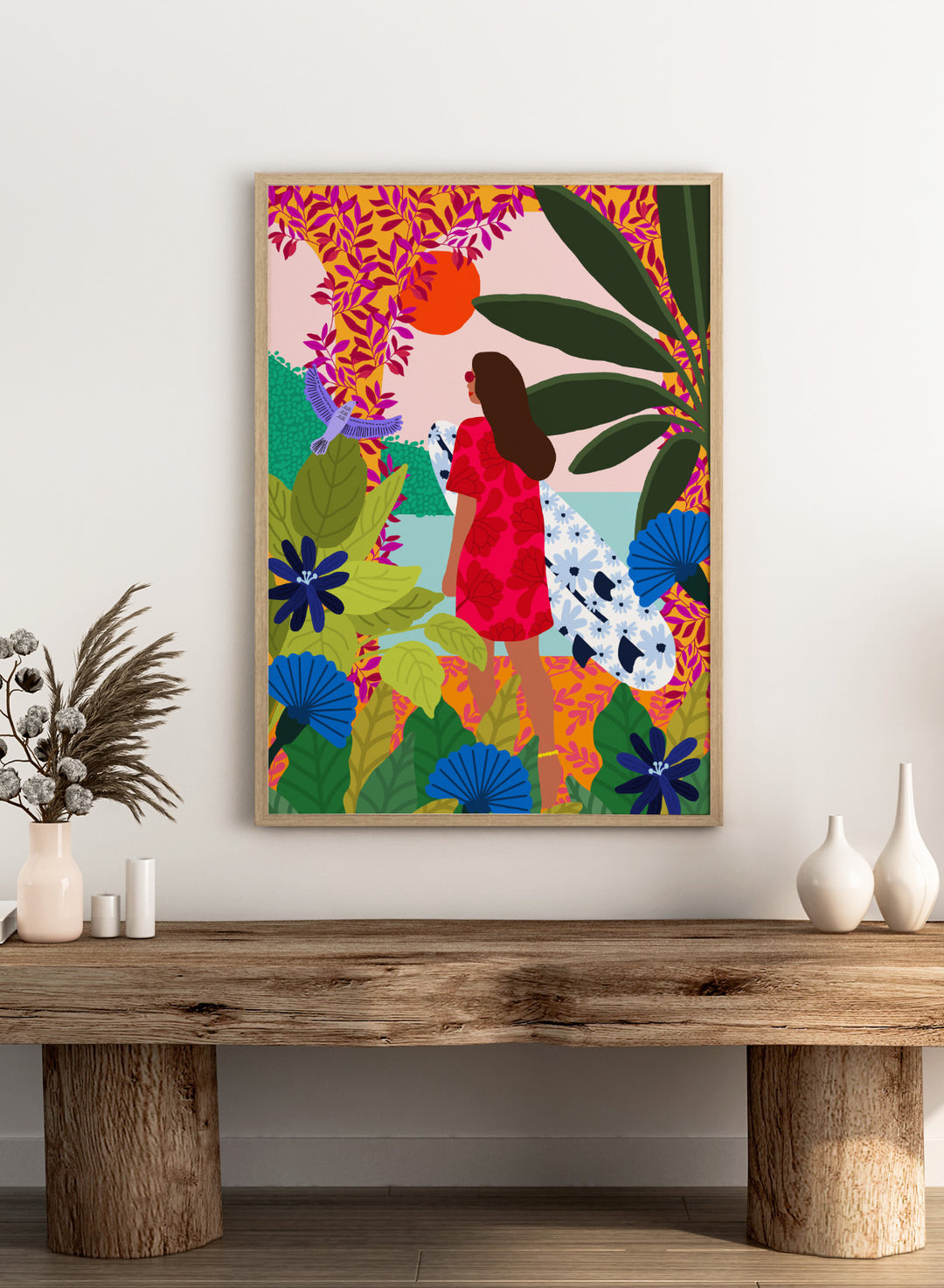 Woman in a red dress with a white surfboard amidst tropical foliage and flowers. Going Surfing by Rafaela Mascaro is a colorful tropical art print featuring a surfer, lush botanicals, vibrant florals, and sunny coastal inspiration.
