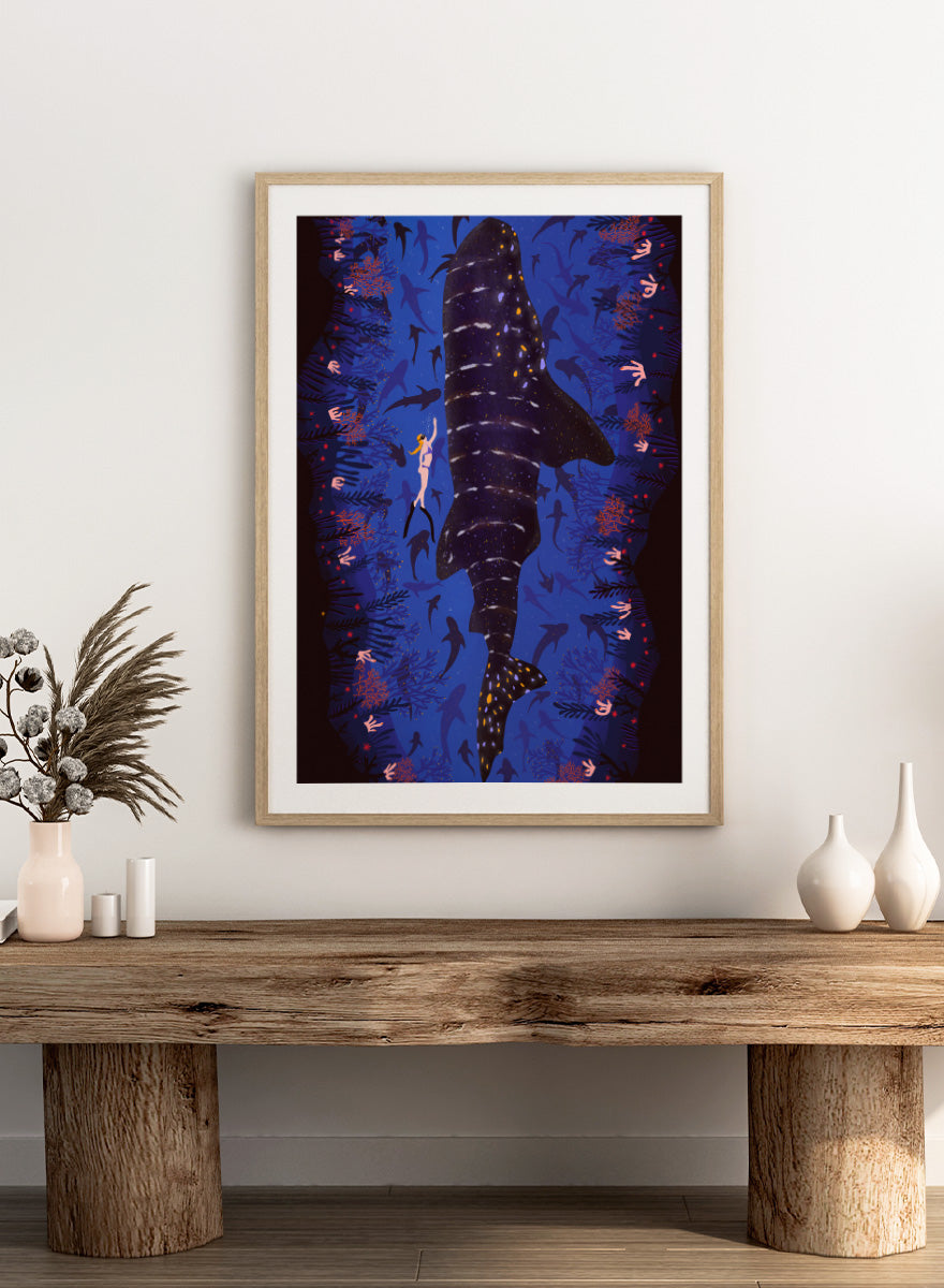 An illustrated art print featuring a large whale shark swimming through a deep blue ocean filled with smaller fish and coral. Diver and Whale Shark art print by Ceyda Alasar features a dramatic underwater view with a whale shark, diver, coral, and rich ocean blues.