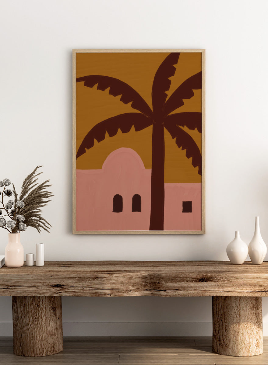 A stylized painting of a palm tree in front of a pink building under a mustard yellow sky. Desert Palm Abode by The Art Concept art print featuring a pink desert home, oversized palm tree, ochre sky, and warm retro color palette.