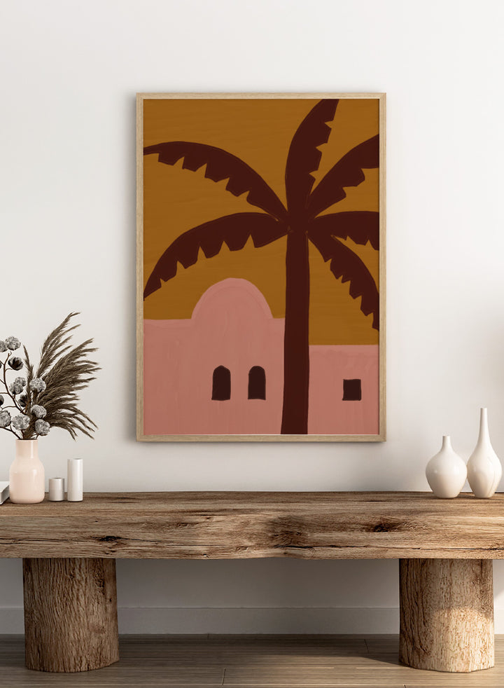 A stylized painting of a palm tree in front of a pink building under a mustard yellow sky. Desert Palm Abode by The Art Concept art print featuring a pink desert home, oversized palm tree, ochre sky, and warm retro color palette.